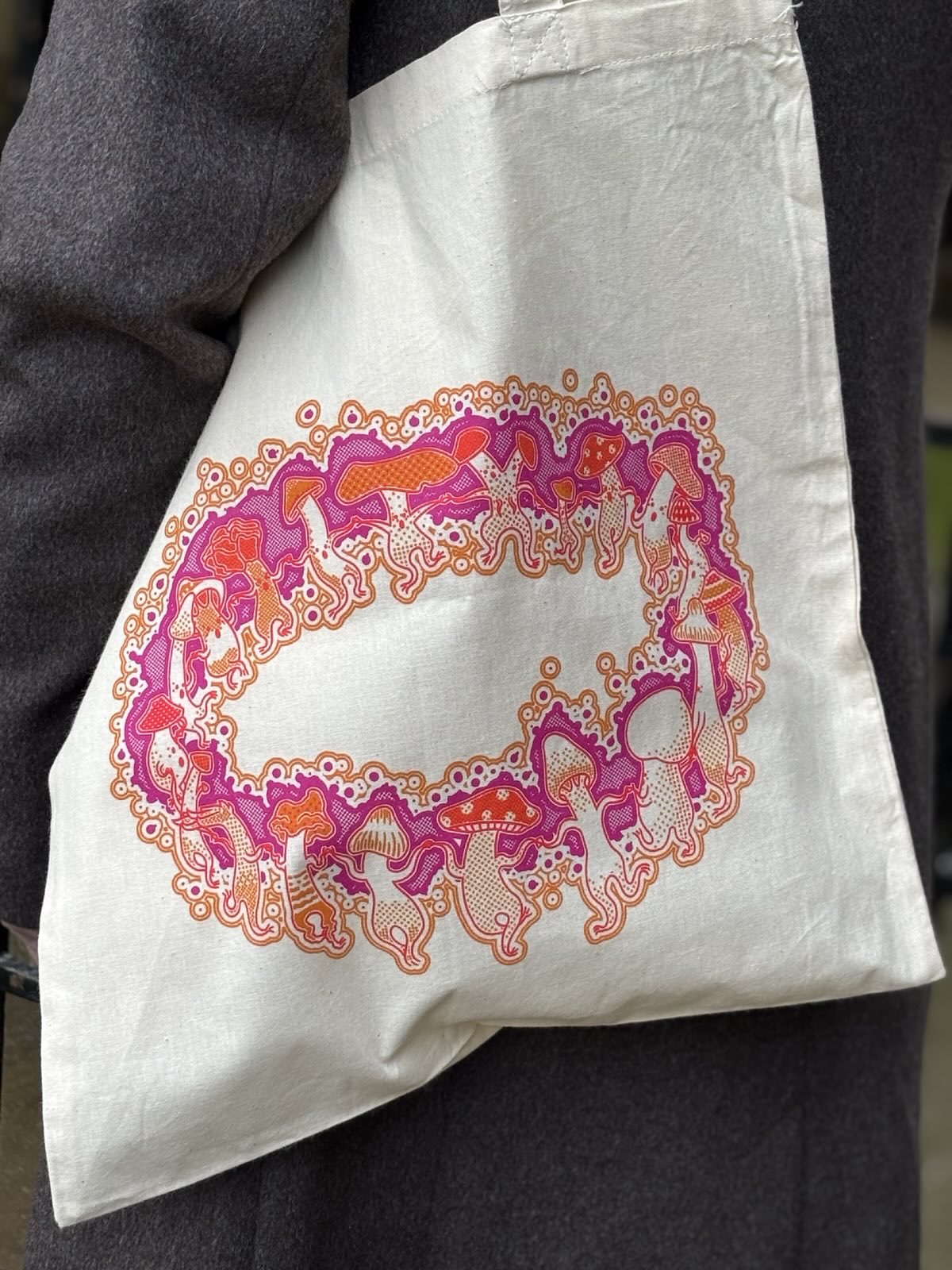 Off-white tote bag with colorful design held by a person wearing a dark jacket.