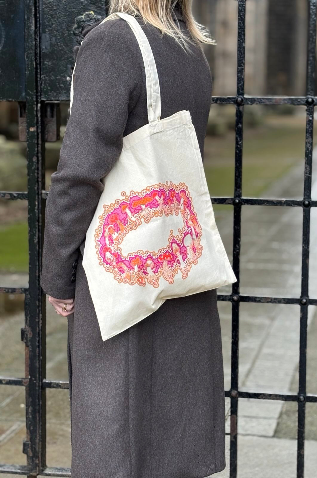 Person wearing a tote bag with a colorful design in front of a metal gate.