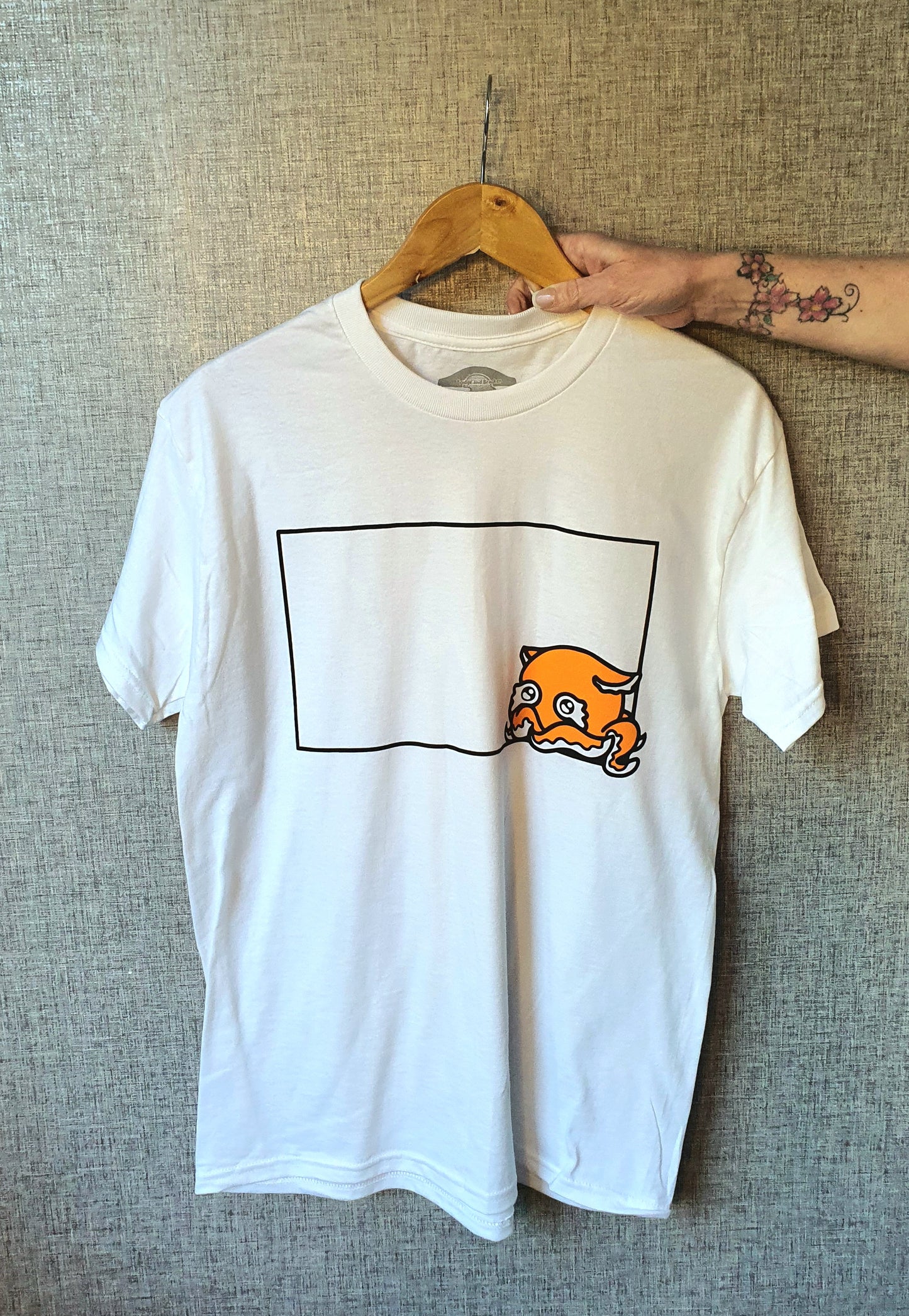 White t-shirt with a graphic design on a hanger against a textured wall.