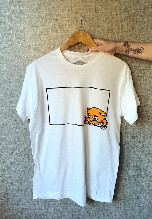 White t-shirt with a graphic design on a hanger against a textured wall.