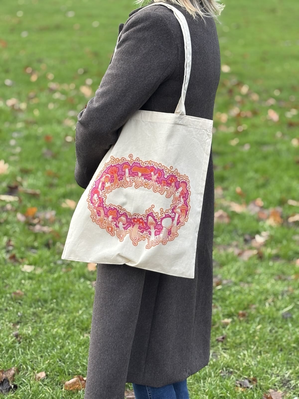 Person holding a tote bag with a colorful design on a grassy background