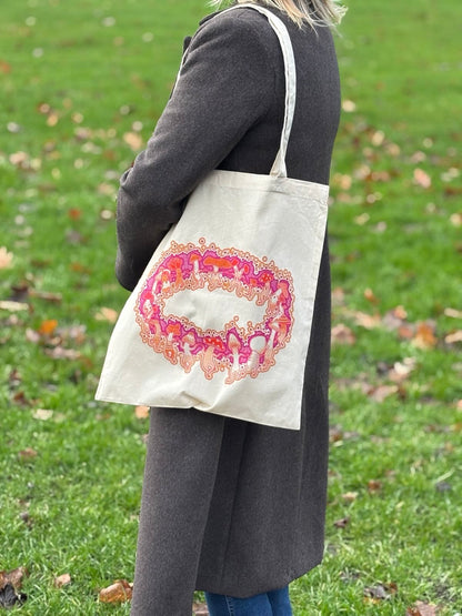 Person holding a tote bag with a colorful design on a grassy background
